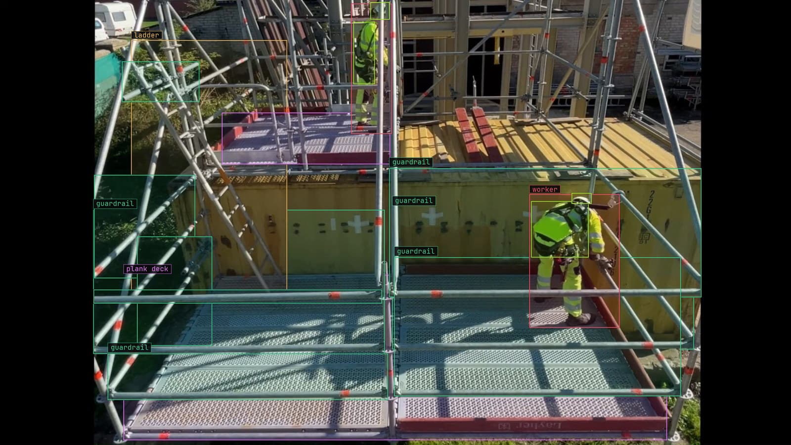 Worker on a scaffold deck, hard hat and fall-arrest gear boxed, from a customer site camera