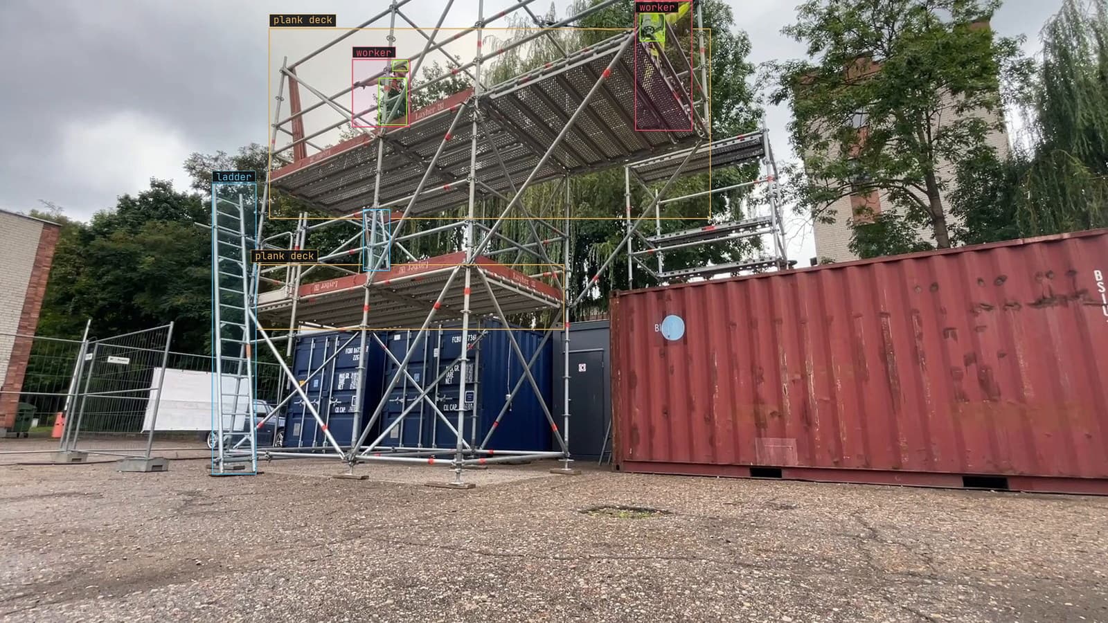 Scaffold tower beside site containers with workers, ladders and plank decks boxed, from a customer site camera