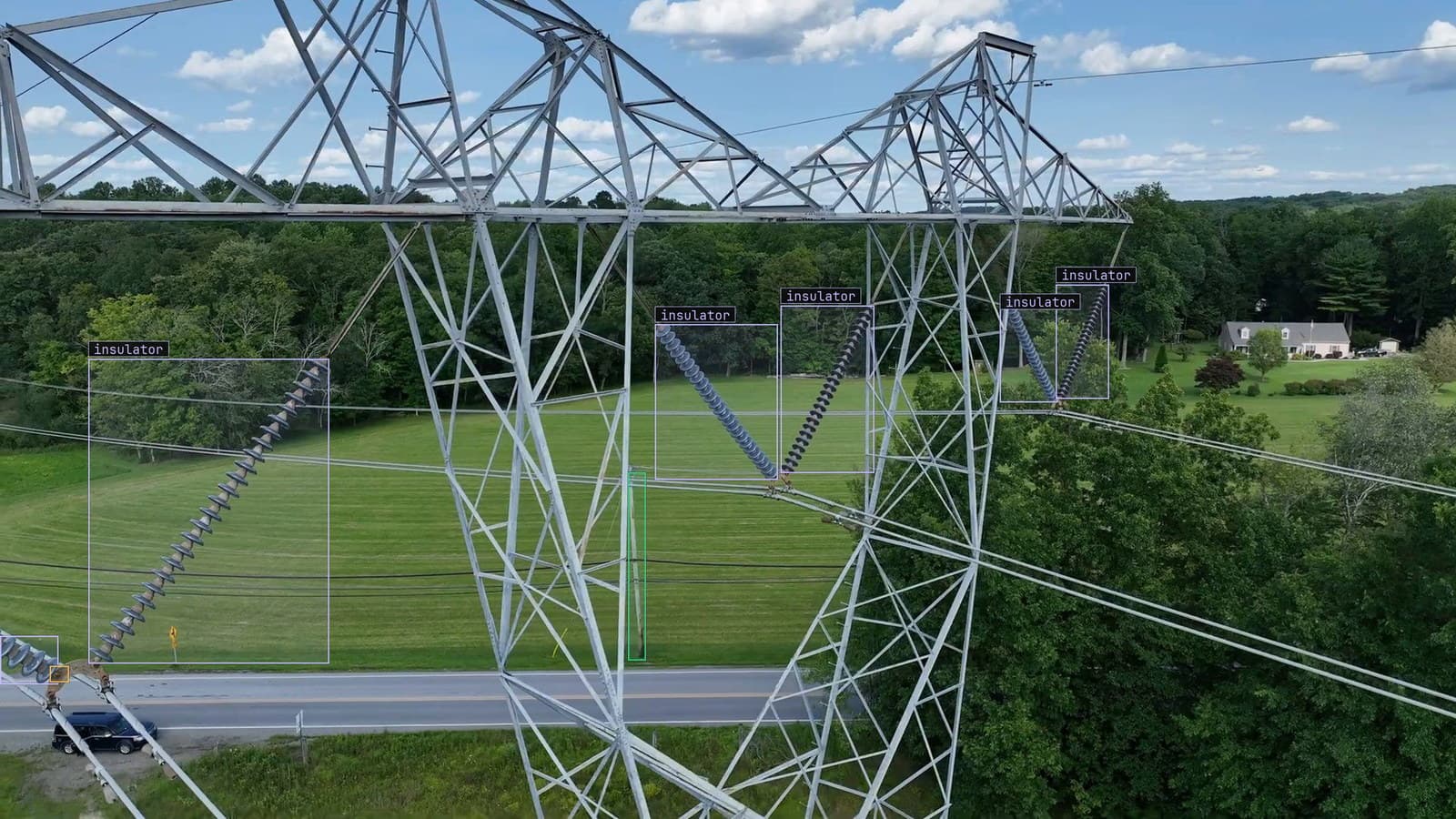 Transmission tower over a country road from a drone, six insulator strings and one corrosion mark boxed, from a customer inspection run