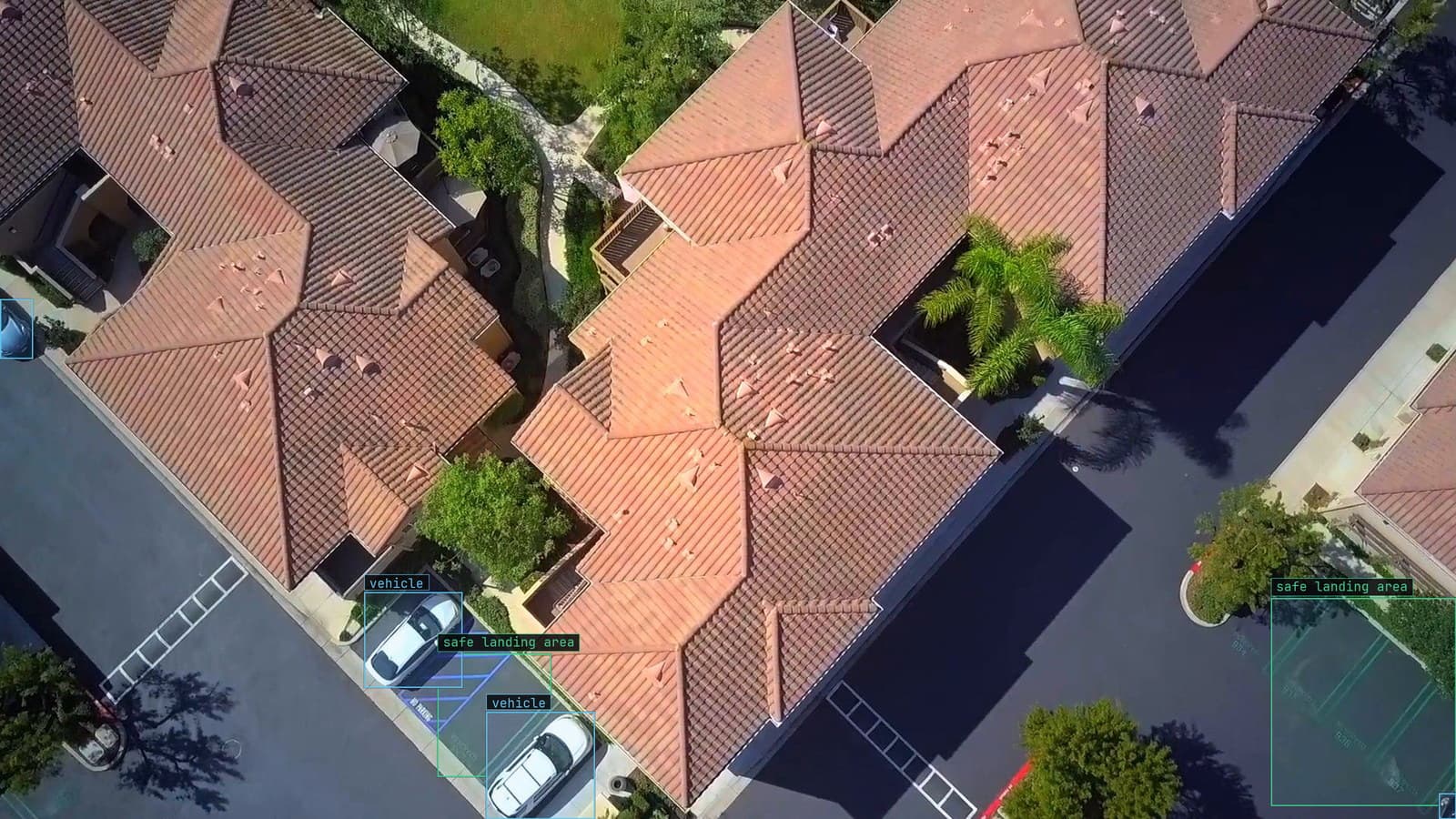 Parked vehicles boxed beside driveways from above, landing areas marked, from a customer drone run