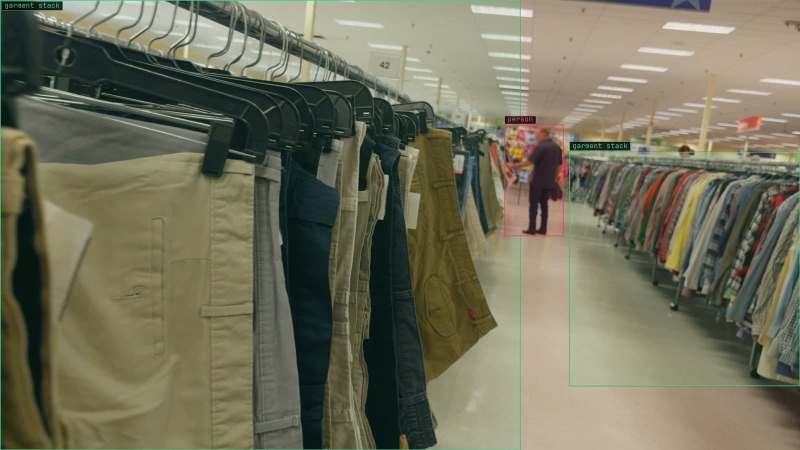 Rack scan down a clothing aisle after a seasonal reset, garment stacks boxed, from a customer store camera